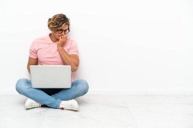 Genç, beyaz arka planda laptopuyla yerde oturan beyaz bir adam...