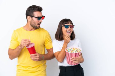 Beyaz arka planda 3 boyutlu gözlüklü ve koca bir kova patlamış mısırı tutan genç bir çift.
