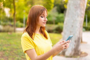 Dışarıdaki güzel kızıl saçlı kadın cep telefonuyla mesaj ya da e-posta yolluyor.