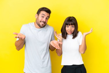 Sarı arka planda yalnız yaşayan genç çift ellerini ve omuzlarını kaldırırken şüphe duyuyorlar.