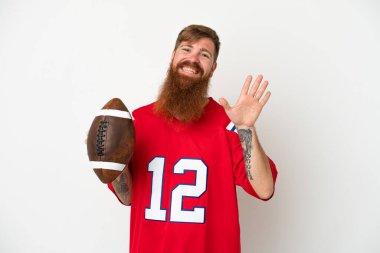 Beyaz arka planda ragbi oynayan Kafkasyalı genç adam mutlu bir ifadeyle selam veriyor.