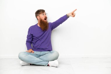 Beyaz arka planda izole bir şekilde yerde oturan beyaz tenli genç adam...