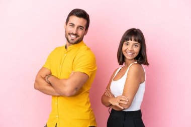 Pembe arka planda izole edilmiş genç bir çift kollarını yan pozisyonda tutarken gülümsüyor.