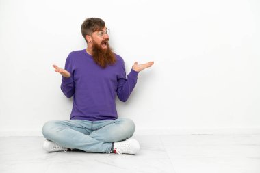 Beyaz arka planda, yerde oturan beyaz tenli, beyaz yüzlü, şaşırtıcı bir yüz ifadesiyle...