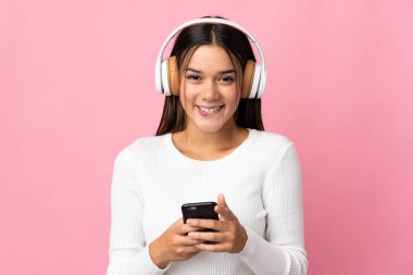 Genç kız mavi arka planda izole edilmiş. Cep telefonuyla müzik dinliyor ve ön tarafa bakıyor.