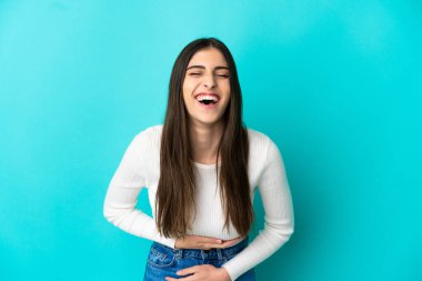 Mavi arka planda izole edilmiş genç beyaz kadın çok gülümsüyor.