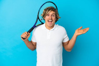 Sarışın tenisçi adam mavi arka planda izole edilmiş ve şok olmuş yüz ifadesi var.