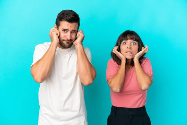 Mavi arka planda izole edilmiş genç bir çift iki kulağını da elleriyle kapatıyor.