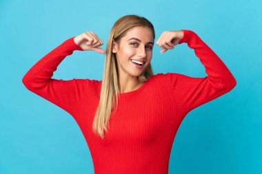 Mavi arka planda izole edilmiş genç sarışın kadın güçlü hareketler yapıyor.