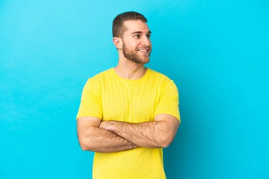 Mavi arka planda izole edilmiş yakışıklı beyaz adam mutlu ve gülümsüyor.