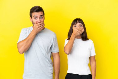 Sarı arka planda izole edilmiş genç bir çift uygunsuz bir şey söyledikleri için ağızlarını ellerle kapatıyor.