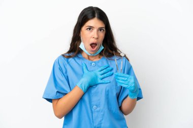 Dişçi kadın beyaz arka planda aletleri tutuyor sağa bakarken şaşırmış ve şok olmuş.