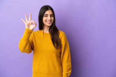 Mor arka planda izole edilmiş beyaz bir kadın parmaklarıyla tamam işareti gösteriyor.