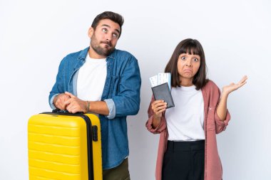 Beyaz arka planda izole edilmiş bavul ve pasaport taşıyan genç bir çift omuzlarını kaldırırken şüpheyle hareket ediyorlar.