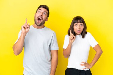 Sarı arka planda izole edilmiş genç bir çift, bir fikir üzerinde parmak kaldırmayı düşünüyorlar.
