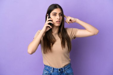 Mor arka planda izole edilmiş cep telefonu kullanan beyaz bir kadın. Şüpheleri ve düşünceleri var.