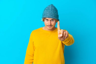 Mavi arka planda izole edilmiş yakışıklı sarışın adam ciddi bir ifadeye sahip birini sayıyor.