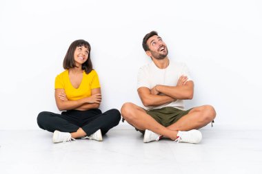 Yerde oturan genç çift beyaz arka planda izole edilmiş gülümserken yukarı bakıyor.