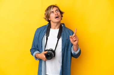 Genç fotoğrafçı sarı arka planda izole edilmiş.