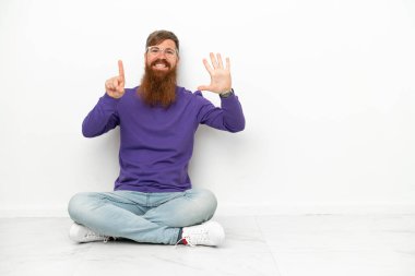 Beyaz arka planda izole bir şekilde yerde oturan Kafkasyalı genç adam parmaklarıyla altı kişi sayıyor.