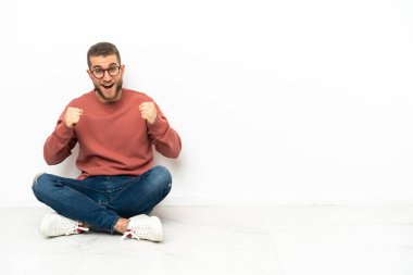 Genç yakışıklı adam yerde oturmuş zaferi kutluyor.