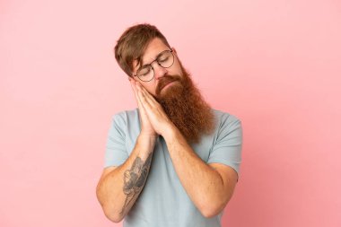Pembe arka planda izole edilmiş genç, kızıl beyaz bir adam uyku jesti yapıyor.