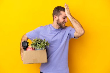 Beyaz tenli genç, sarı arka planda izole edilmiş eşyalarla dolu bir kutuyu alırken bir şey fark etti ve çözümü bulmaya çalışıyor.