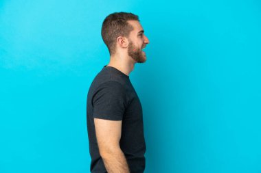 Mavi arka planda izole edilmiş yakışıklı beyaz adam yan yana gülüyor.