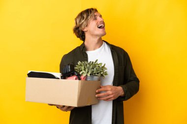 Sarışın adam, sarı arka planda izole edilmiş şeylerle dolu bir kutuyu kaldırırken hareket ediyor.