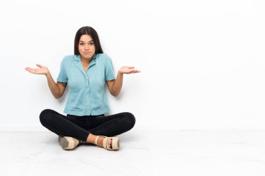 Genç bir kız yerde oturuyor ve ellerini kaldırırken şüphe duyuyor.