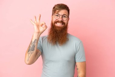 Pembe arka planda izole edilmiş genç, beyaz bir adam parmaklarıyla tamam işareti gösteriyor.