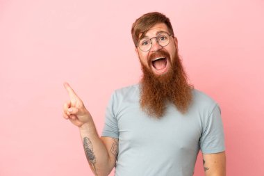 Pembe arka planda izole edilmiş genç, kızıl, beyaz adam şaşırmış ve işaret ediyor.