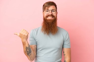 Pembe arka planda izole edilmiş genç beyaz adam bir ürünü sunmak için yan tarafı işaret ediyor.