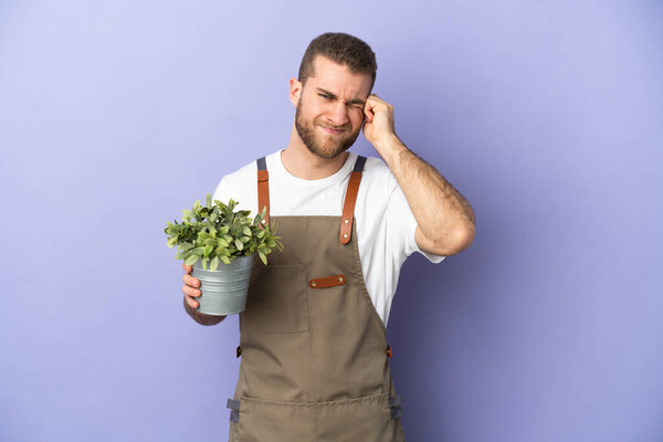 Gardener caucasian man holding a plant isolated on yellow background frustrated and covering ears