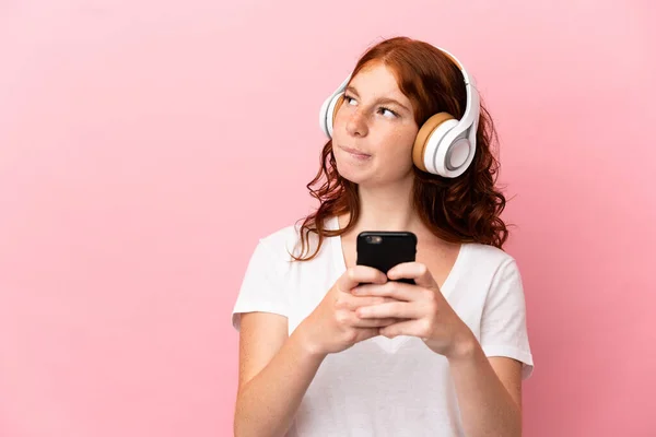 Adolescente Donna Rossastra Isolata Sfondo Rosa Ascoltare Musica Con Cellulare — Foto Stock