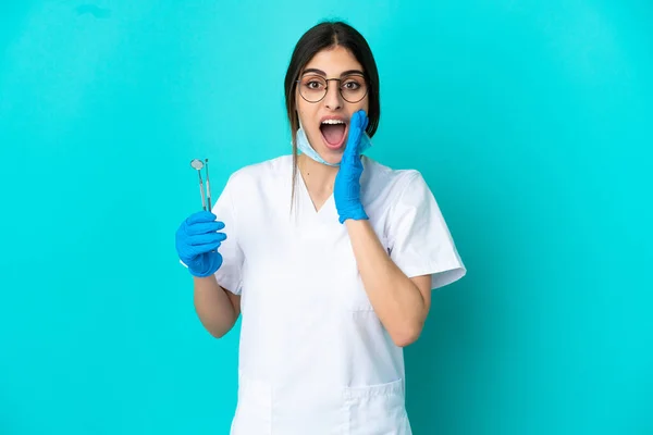 年轻的高加索牙医妇女拿着用蓝色背景隔离的工具 脸上带着惊讶和震惊的表情 — 图库照片