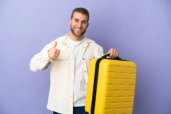 若いですハンサムなCaucasian男隔離上の紫の背景で休暇で旅行スーツケースとととともに親指アップ — ストック写真