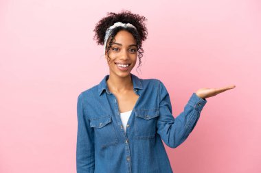 Pembe arka planda izole edilmiş genç Latin bir kadın bir ilan vermek için avucunun içinde hayali bir alan tutuyor.