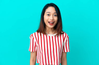 Genç Vietnamlı kadın, mavi arka planda izole edilmiş, şaşırmış bir yüz ifadesi var.