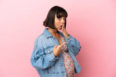 Soyutlanmış pembe arka planda genç hamile bir kadın. Sürpriz bir ifadeyle.