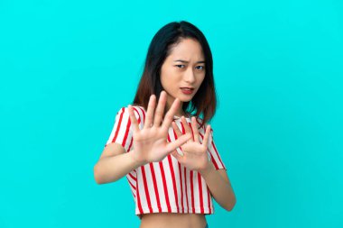 Genç Vietnamlı kadın mavi arka planda izole edilmiş, gergin ellerini öne doğru uzatıyor.