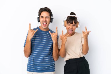 Beyaz arka planda izole edilmiş genç melez arkadaşlar rock hareketleri yaparak müzik dinliyorlar.