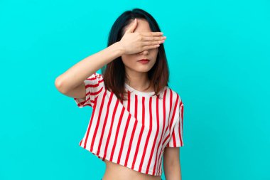 Genç Vietnamlı kadın mavi arka planda izole edilmiş, gözleri elle kaplanmış. Bir şey görmek istemiyorum.