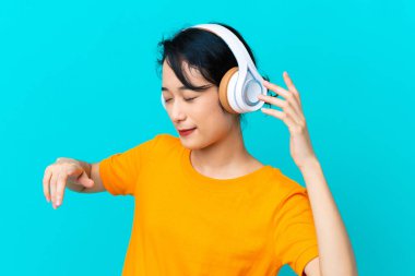 Genç Vietnamlı kadın mavi arka planda izole edilmiş müzik ve dans dinliyor.