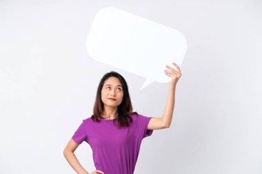 Beyaz arka planda izole edilmiş genç Vietnamlı kadın boş bir konuşma balonu tutuyor ve düşünüyor.