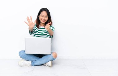 Yerde dizüstü bilgisayarı olan genç Vietnamlı kadın beyaz duvarda tecrit edilmiş, parmaklarıyla altı kişi sayıyor.