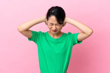 Pembe arka planda izole edilmiş genç Vietnamlı kadın hayal kırıklığına uğramış ve kulaklarını kapatmış.