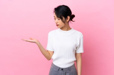 Genç Vietnamlı kadın pembe arka planda izole edilmiş. Kopyalama alanını şüpheyle tutuyor.