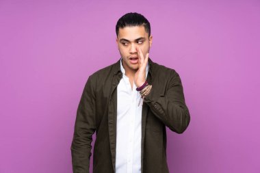 Asyalı yakışıklı adam mavi arka planda izole edilmiş. Yan tarafa bakarken sürpriz bir hareketle bir şeyler fısıldıyor.