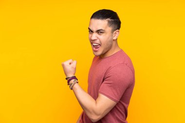 Asyalı yakışıklı adam sarı arka planda izole edilmiş sürpriz bir ifadeyle işaret ederken